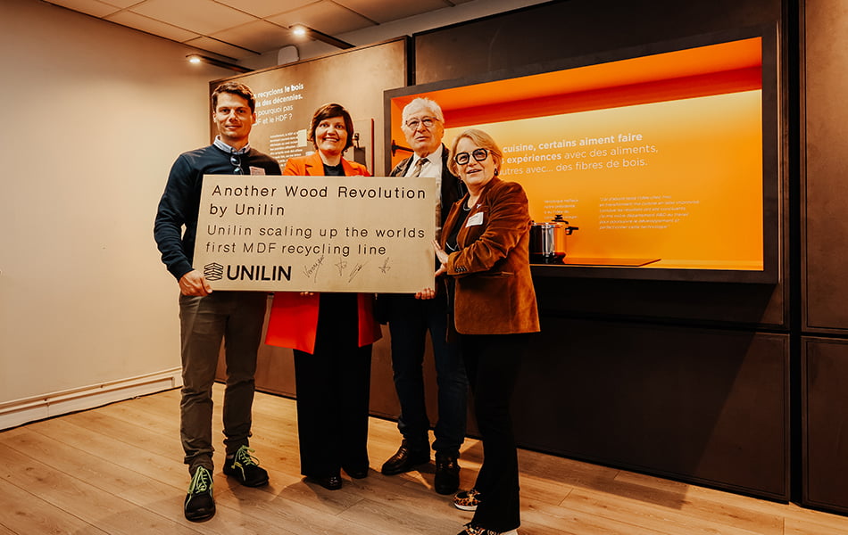 Les collègues d'UNILIN Panels affichent leur fierté et montrent un panneau portant le titre : Une autre révolution du bois par Unilin